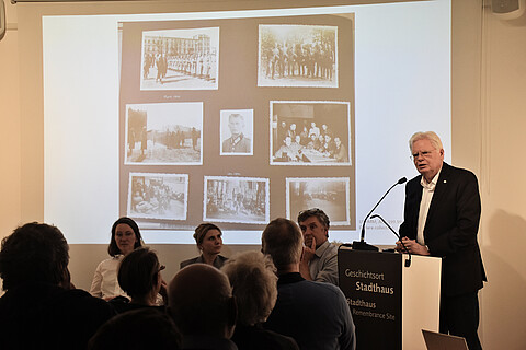 Wolfgang Kopitzsch steht am Pult und spricht, hinter ihm auf einer Leinwand eine Seite aus dem Fotoalbum von Colberg
