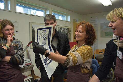 4 Personen, die Schürzen tragen, eine Person hält ein Plakat hoch.