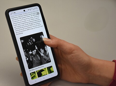 Eine Hand hält ein Handy auf dem Webseite aufgerufen ist.