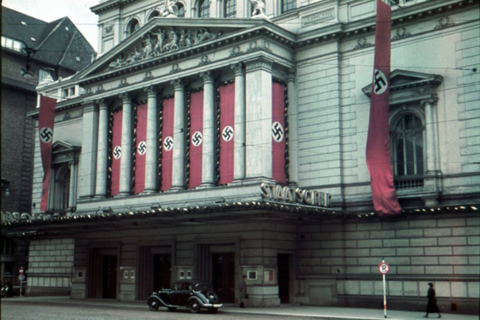 Die Hamburgische Staatsoper an der Dammtorstraße mit Hakenkreuzbeflaggung zwischen den Säulen des Haupteingangs, ca. 1937. Das mit Hakenkreuzfahnen beflaggte Vorderhaus wurde 1943 bei einem Luftangriff zerstört und 1955 durch einen Neubau ersetzt.