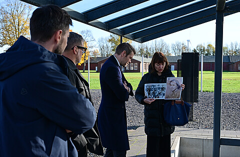 Paula Scholz gibt eine kurze Information zum Thema Fußball(er) im KZ, dazu hält sie zwei Fotografien hoch während drei Personen auf sie schauen