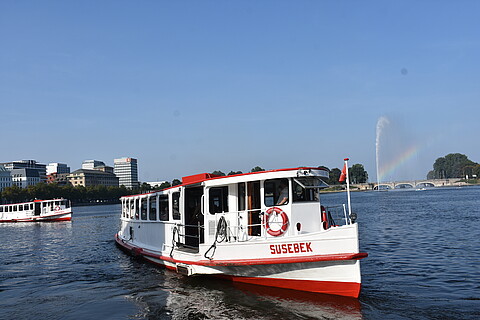 Die Alternative Alsterkanalfahrt startet an der Binnenalster. Eine weiße Barkasse auf blauem Wasser bei Sonnenschein 