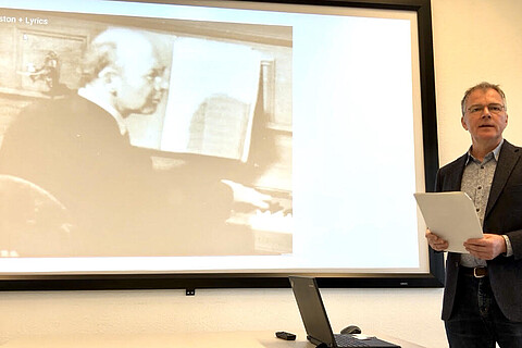 Hanno Billerbeck vor einer Leinwand während seines Vortrags zu Charles Amberg