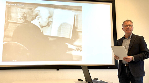 Hanno Billerbeck vor einer Leinwand während seines Vortrags zu Charles Amberg