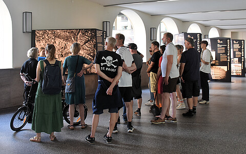 Die Rücken einer Gruppe von Personen, auf einen Tshirt ist das St. Pauli Logo zu sehen.