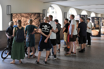Die Rücken einer Gruppe von Personen, auf einen Tshirt ist das St. Pauli Logo zu sehen.