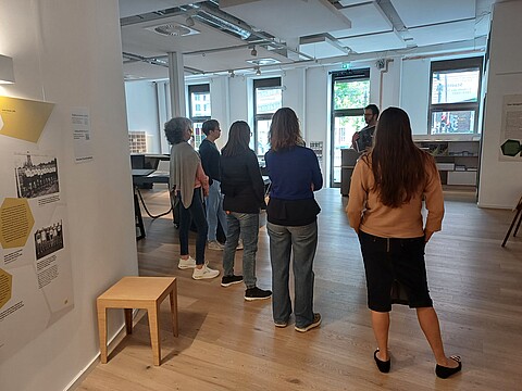 Rücken von Menschen, im Vordergrund Tafeln einer Ausstellung