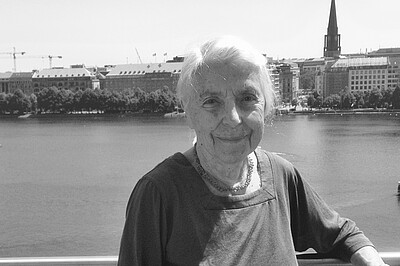 Brigitte Alexander steht bei ihrem letzten Besuch in Hamburg auf einem Balkon, hinter ihr die Binnenalster.9