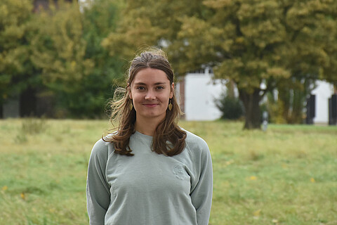 Marie Zachger steht zentral im Bild. Im Hintergrund sieht man eine grüne Wiese.