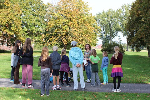 Kinder stehen um einen Guide herum, im Hintergund das Klinkerwerk und Bäume.