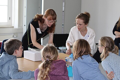 Kinder und Archivarin versammeln sich um eine Archivbox.