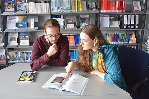 Gabriel und Uliana sitzen an einem Tisch in der Bibliothek der KZ-Gedenkstätte Neuengamme und schauen gemeinsam in ein Buch