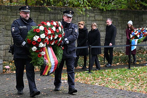 Zwei Polizisten gehen mit einem Kranz voraus