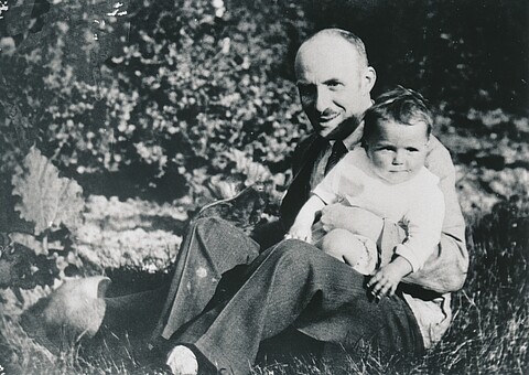 Fritz Solmitz sitzt mit seiner Tochter Brigitte als Kleinkind auf seinem Schoß auf dem Rasen eines Gartens, 1929