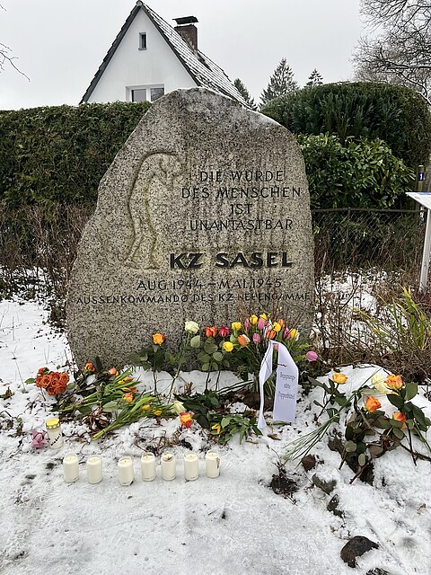 Man sieht den Gedenkstein des KZ-Außenlagers Sasel, vor dem Blumen niedergelegt wurden. 