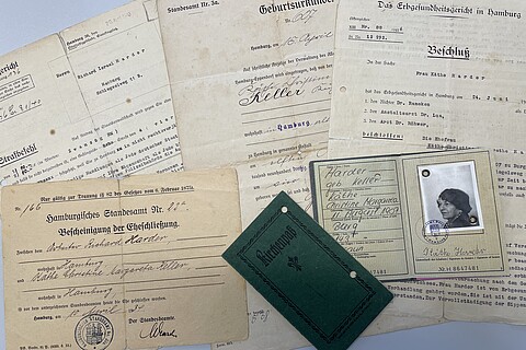 Auf einem Tisch liegen Beispieldokumente aus dem Nachlass, darunter die Bescheinigung der Eheschließung von Käthe und Richard Harder, ein Ausweis und eine Geburtsurkunde von Käthe Harder, ein Strafbefehl gegen Richard Harder und ein Beschluss vom Erbgesundheitsgericht